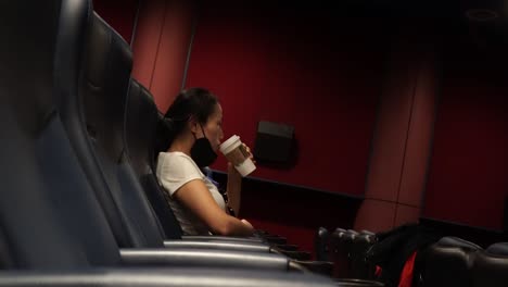 side view of a lone lady drinking coffee while sitting alone in an empty cinema