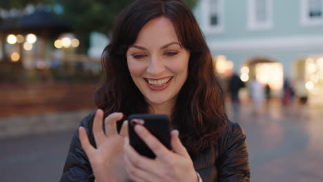retrato de una mujer encantadora, alegre y elegante que usa una aplicación de teléfono inteligente, envía mensajes de texto, navega y disfruta de una tranquila noche urbana