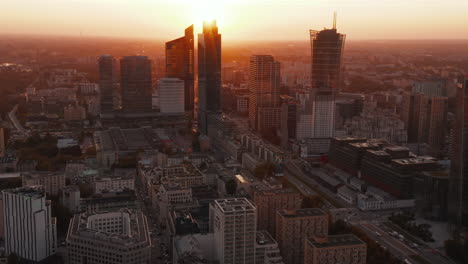 Fly-above-large-city.-Tilt-up-reveal-downtown-skyscrapers-against-bright-sunset-light.-Warsaw,-Poland