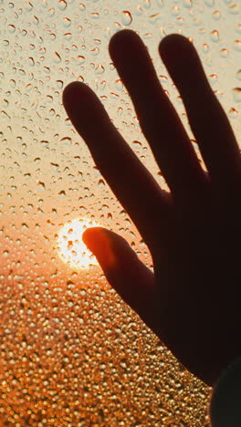 dark silhouette of hand on window with drops at rain closeup. elegant palm expresses heartbreak period touching glass on stormy day. depression disorder