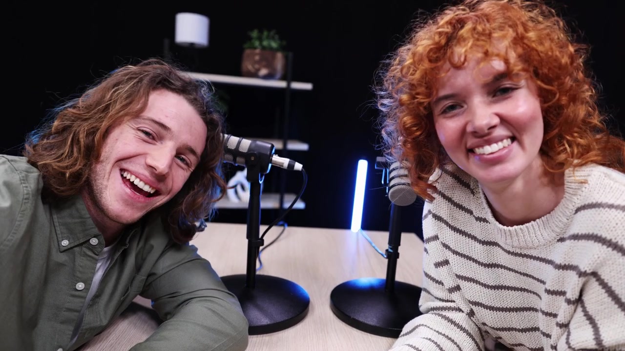 Giovani uomo e donna allegri che salutano e sorridono in uno studio per podcast