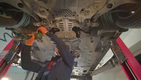 joven mecánico profesional que trabaja bajo el coche moderno levantado en el servicio de reparación de automóviles. servicio de automóviles, mantenimiento de reparación.