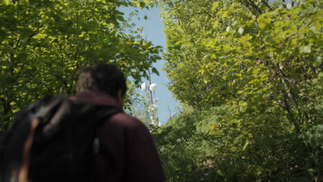 camera following a young hiker approaching a peak of mountain among green trees on rocky path