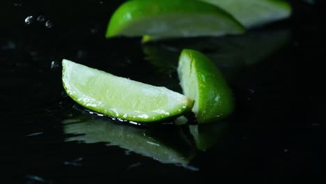 Lime-slice-on-black-studio-background-with-water,-close-up-view