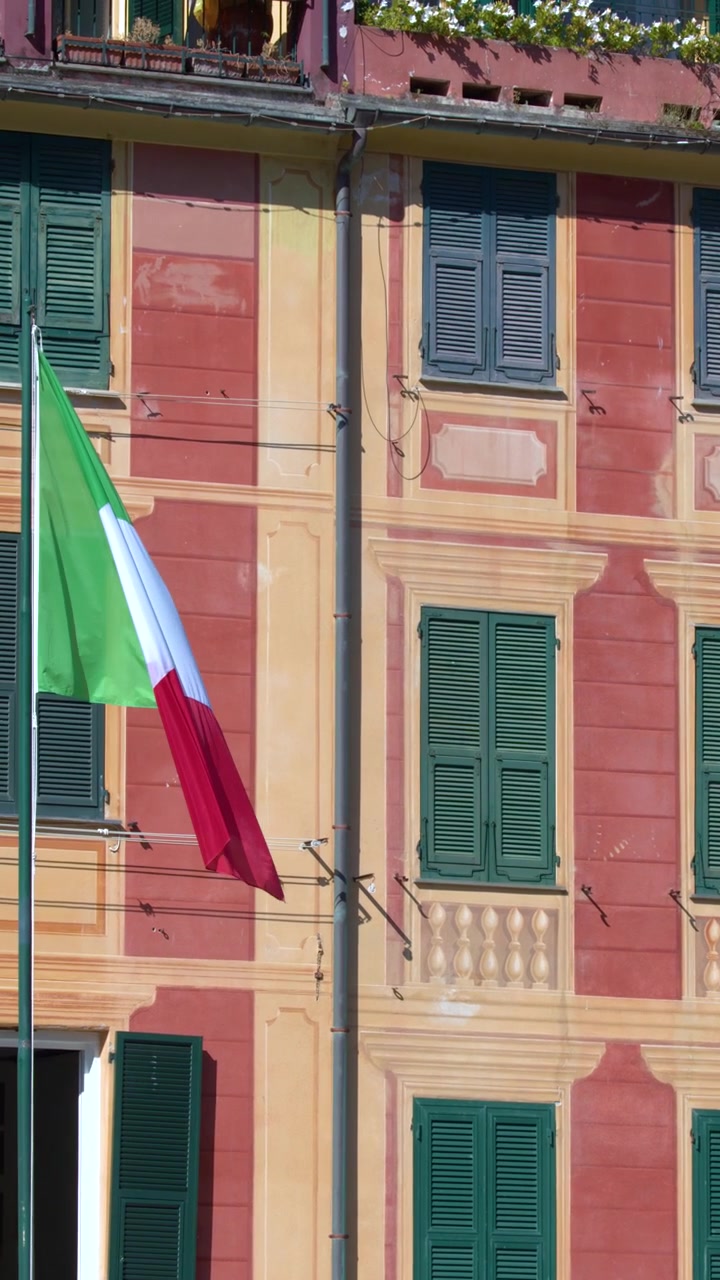 Panorâmica vertical sobre arquitetura mediterrânea vibrante com balões verdes e uma bandeira nacional italiana tremulando.