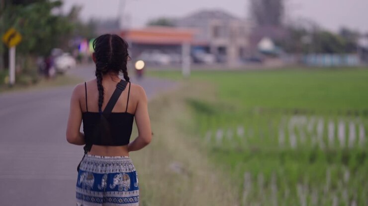 A young woman walks on a rural road next to a rice field