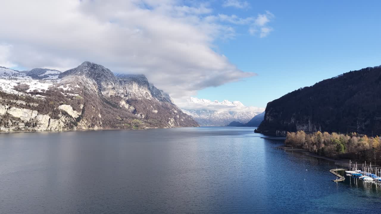 Expansive, tranquil winter panorama of Klöntalersee, Glarus, Switzerland. The towering, snow-covered Klöntal peaks are sharply reflected in the still, dark blue lake water. Cold, alpine splendor