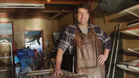 caucasian male knife maker in workshop, looking at camera and smiling