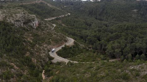 aerial shot of a campervan or motorhome all alone on a winding road through a forest in spain