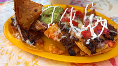 eating traditional tex-mex mexican nachos with beef chilli con carne, guacamole, melted cheese and sour cream, totopos tortilla chips, tasty food, 4k shot