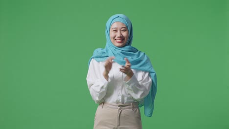 아시아 여성 이 녹색 스크린 배경 스튜디오 에 서 있는 동안 미소 짓고 손 을 박수 를 치고 있다