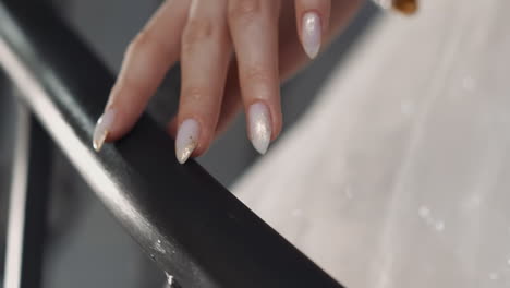 bride with elegant manicure in white dress touches railing