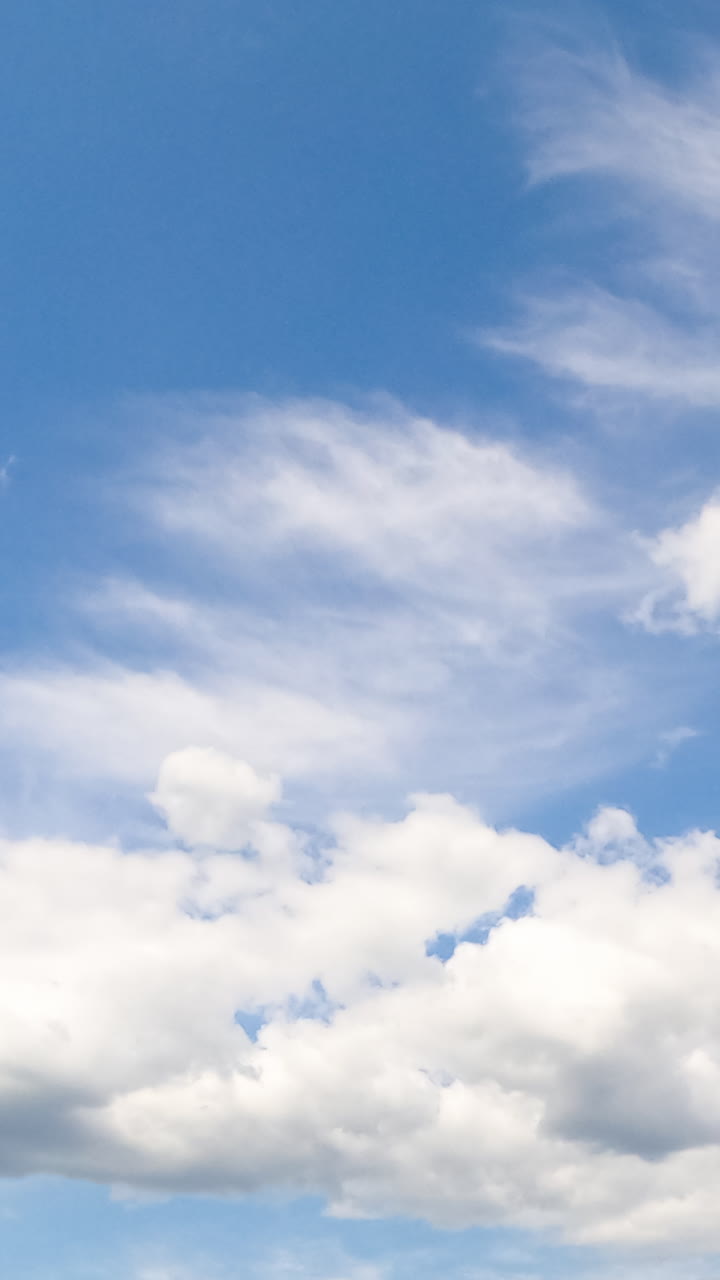 Cumulus and cirrus clouds in the blue sky. White cloudscape in the bright light of the summer sun. Timelapse. Vertical video