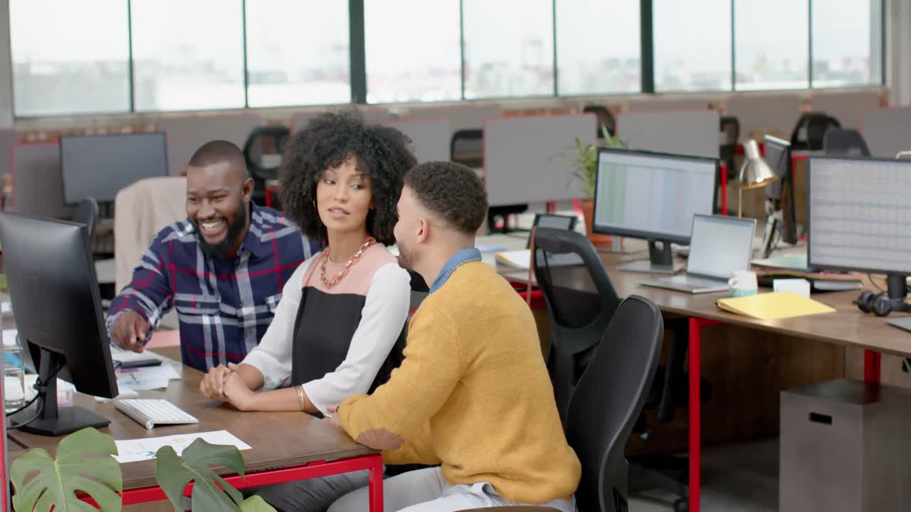 Three happy diverse colleagues discussing over a computer at office