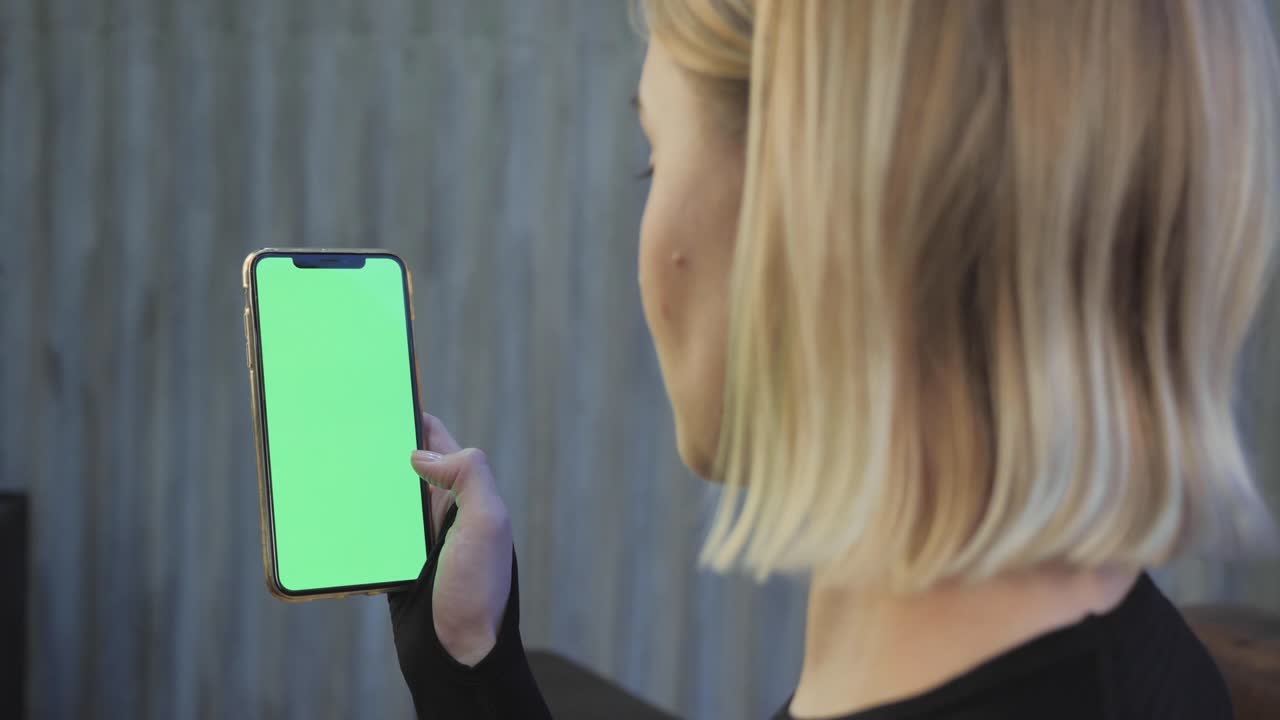 una joven atlética sostiene un teléfono inteligente en la mano, muestra una pantalla chromakey verde, está en el gimnasio