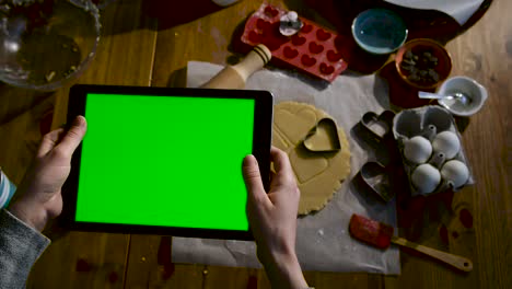 woman watching video from tablet in hand in the kitchen, watching cake or cookie recipe videos. green screen tablet.