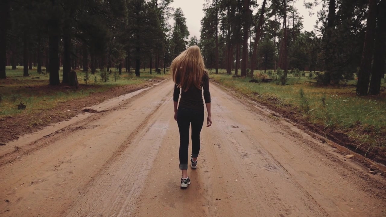 Young Woman Walking on a Dirt Road in a Forest