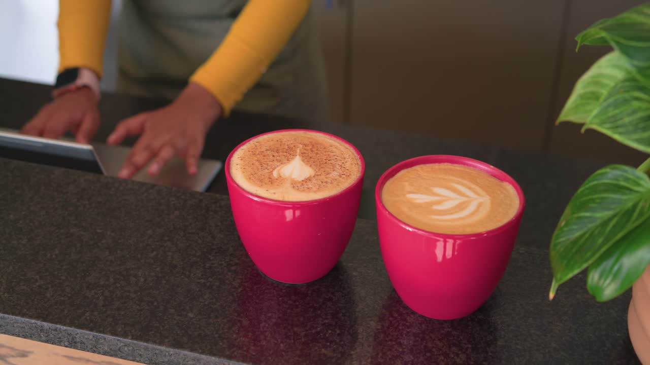 Barista in grembiule verde che sistema tazze rosse, tocca un tablet ed elabora un ordine al bancone di un bar