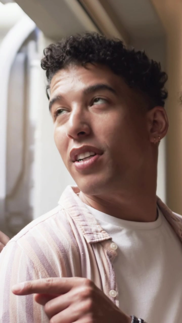 Vertical video: Turning man with hoop in striped top at home seeing motion outside window pointing