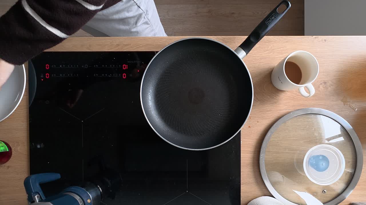 A top-down shot captures the process of making pancakes in a frying pan on an electric stove. The warm lighting creates a cozy atmosphere, showcasing the detailed view of golden pancakes