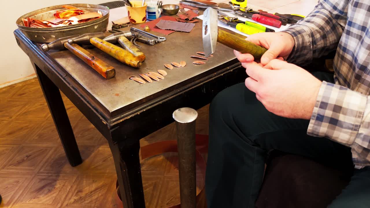 Coppersmith flattening small copper pieces to make traditional earrings by hand with hammer.