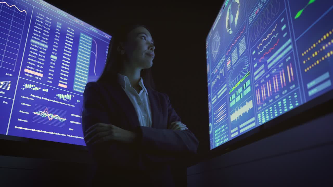 The businesswoman standing near the blue screens in the dark lab