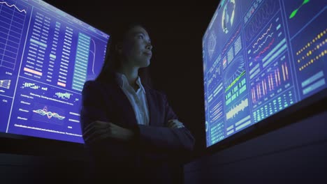 the businesswoman standing near the blue screens in the dark lab