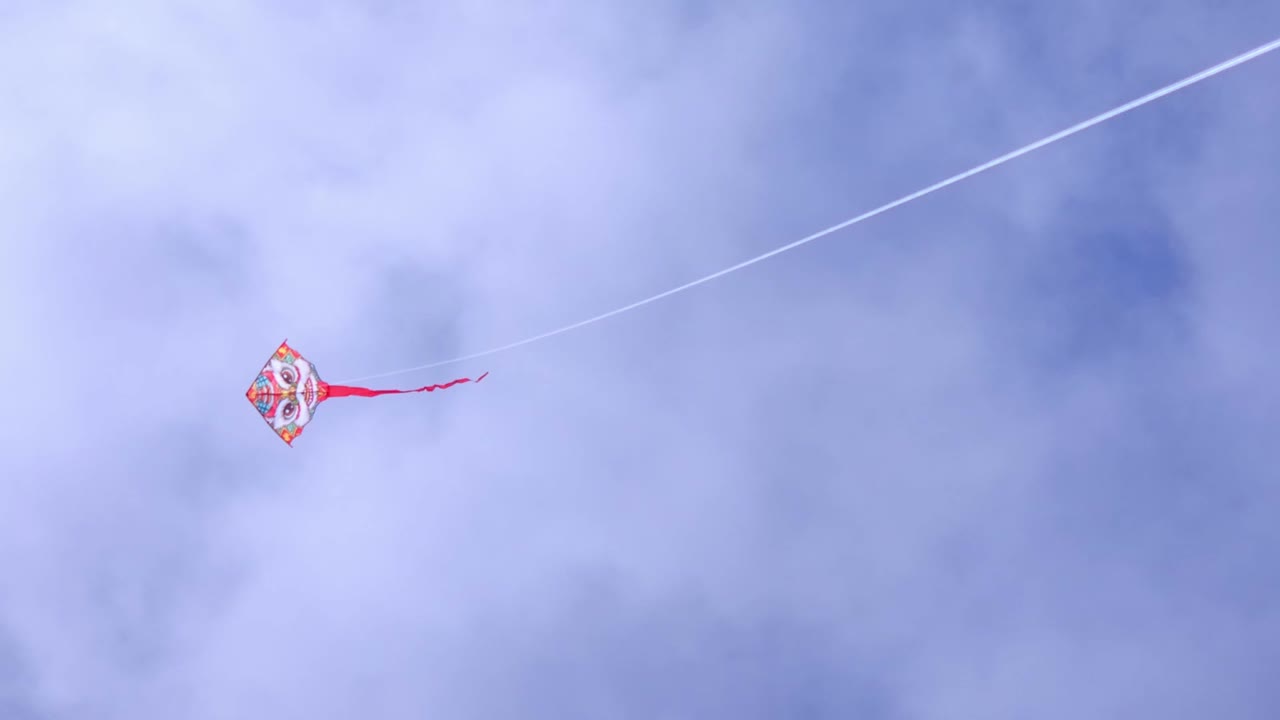 Colorful Kite Flying High Against Blue Cloudy Sky on Breezy Afternoon