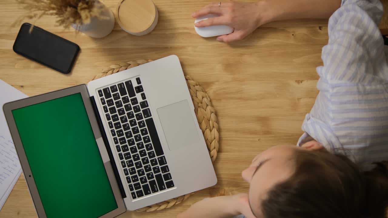Green computer screen. The girl lies at the table and remotely learns, works. Surfs the Internet. A girl in a striped pajama top. Top view