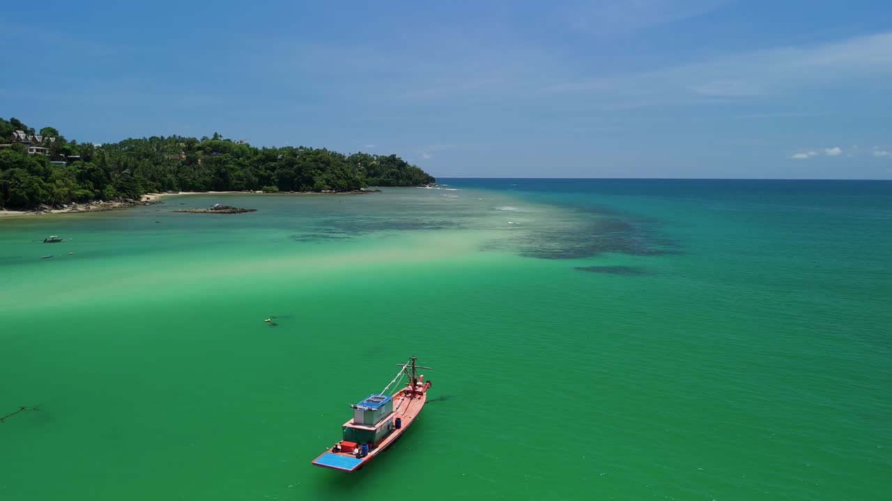 Aerial flyover tracks longtail fishing boats over turquoise Bang Tao Bay, Phuket