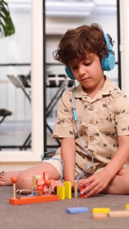 Young boy playing with wooden construction toy while listening music