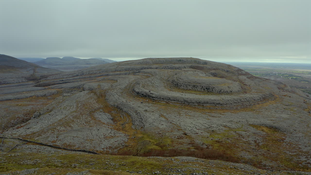 Ascending aerial view of Burren peak on a misty day, highlighting its rocky landscape. County Clare, Ireland
