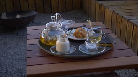 Herbal-tea-in-glass-teapot-with-milk-and-muffin-sitting-on-wood-table