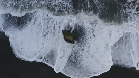 aerial top down black sandy beach and waves crashing against stapavik rock during daytime