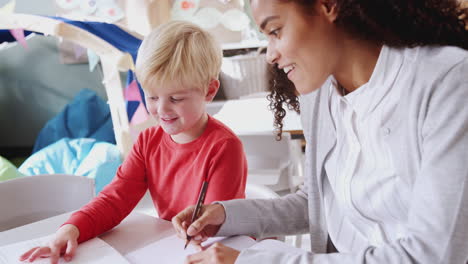 maestra de escuela infantil trabajando uno a uno con un joven escolar blanco, de cerca