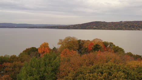 Drone-Aéreo-Rodando-Sobre-Las-Copas-De-Los-árboles-De-Colores-Otoñales,-Hacia-El-Río-Hudson-En-Un-Día-Nublado-En-El-Parque-Croton-Point-Que-Estaba-Vacío