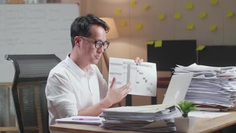 hombre asiático con documentos que explican el trabajo en papel mientras tiene una llamada de video en una computadora portátil en la oficina