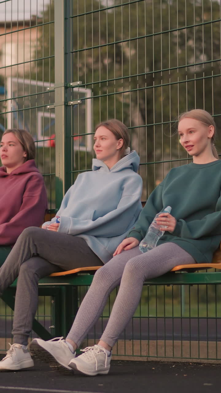 경기장 좌석에 앉아 물병을 들고 있는 여인들의 그룹. 한 여인이 다리를 는 동안 다른 여인은 다리를 앞으로 펴고, 캐주얼한 야외 피트니스 세션을 보여주고 있습니다.