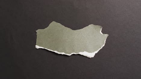 Video-of-close-up-of-torn-piece-of-green-paper-on-black-background