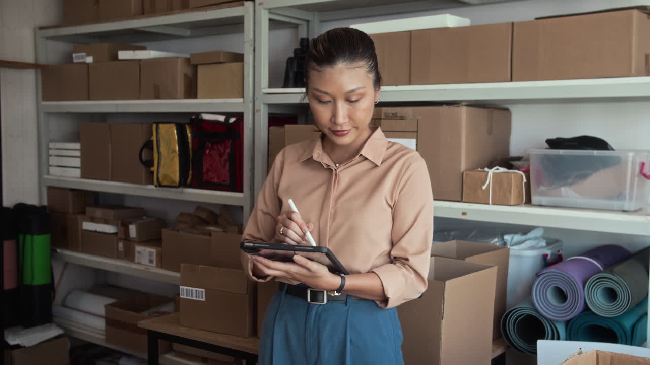 Asian Warehouse Worker Using Tablet while Checking Parcels