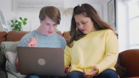 pareja con síndrome de down sentada en el sofá usando una computadora portátil en casa