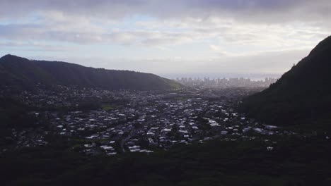 establishing shot of a small residential island town nestled between two rainforest covered mountains with the city view on the horizon in the ravine on the island of oahu hawaii in late afternoon