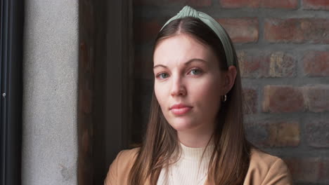 young caucasian businesswoman with brown hair and headband poses near a window