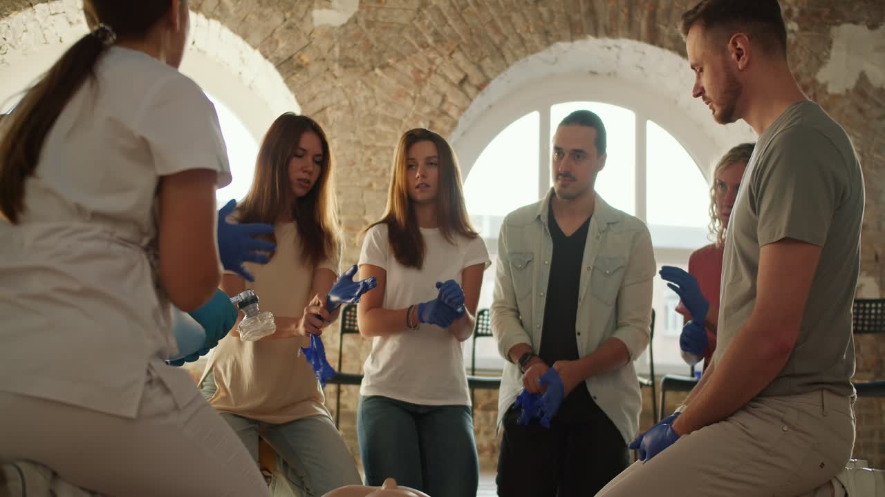 съемки вблизи: группа людей учится у медсестры-врача на медицинском курсе, готовится к практическому уроку и надевает медицинские перчатки