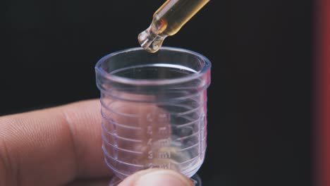 man drops liquid into measuring cup on black background