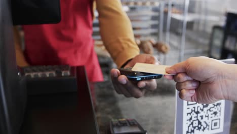 midsection of diverse male baker and female client paying with credit card in bakery, slow motion