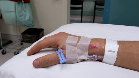 movimientos lentos de la mano de la mano derecha masculina caucásica irreconocible en un escenario médico con iv en la muñeca