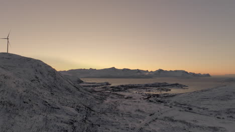 einzelne windkraftanlage dreht sich auf einem berg in der eiskalten, schneebedeckten arktischen landschaft in norwegen