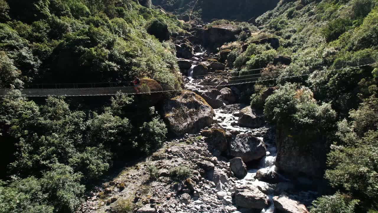 mujer joven caminando por el puente oscilante en copland track, nueva zelanda
