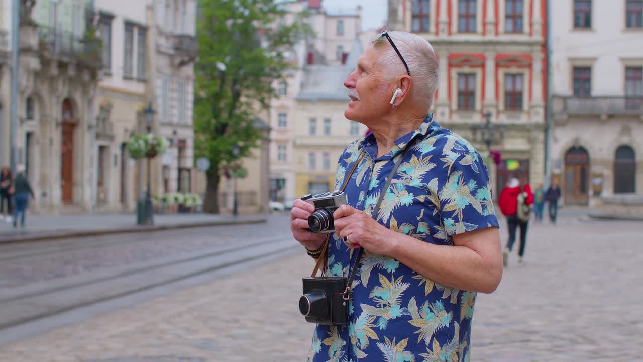 Turista anziano con macchina fotografica retrò che ascolta musica in cuffia ballando all'aperto e divertendosi